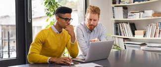 Two people in an office working together at a laptop.